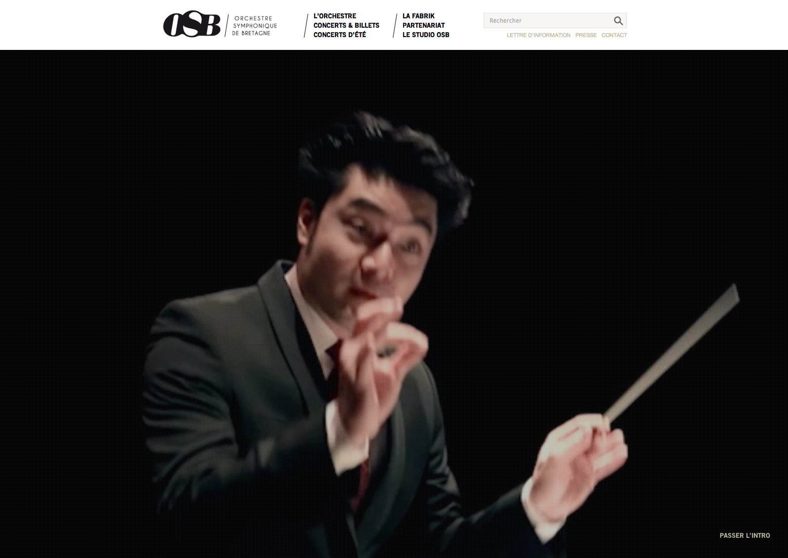 L'image montre un chef d'orchestre en pleine action, vêtu d'un costume sombre, avec un bâton de direction à la main. Son visage exprime une grande concentration et passion, et il semble conduire les musiciens avec dynamisme. L'arrière-plan est flou, mettant en valeur le chef d'orchestre et la scène de concert.