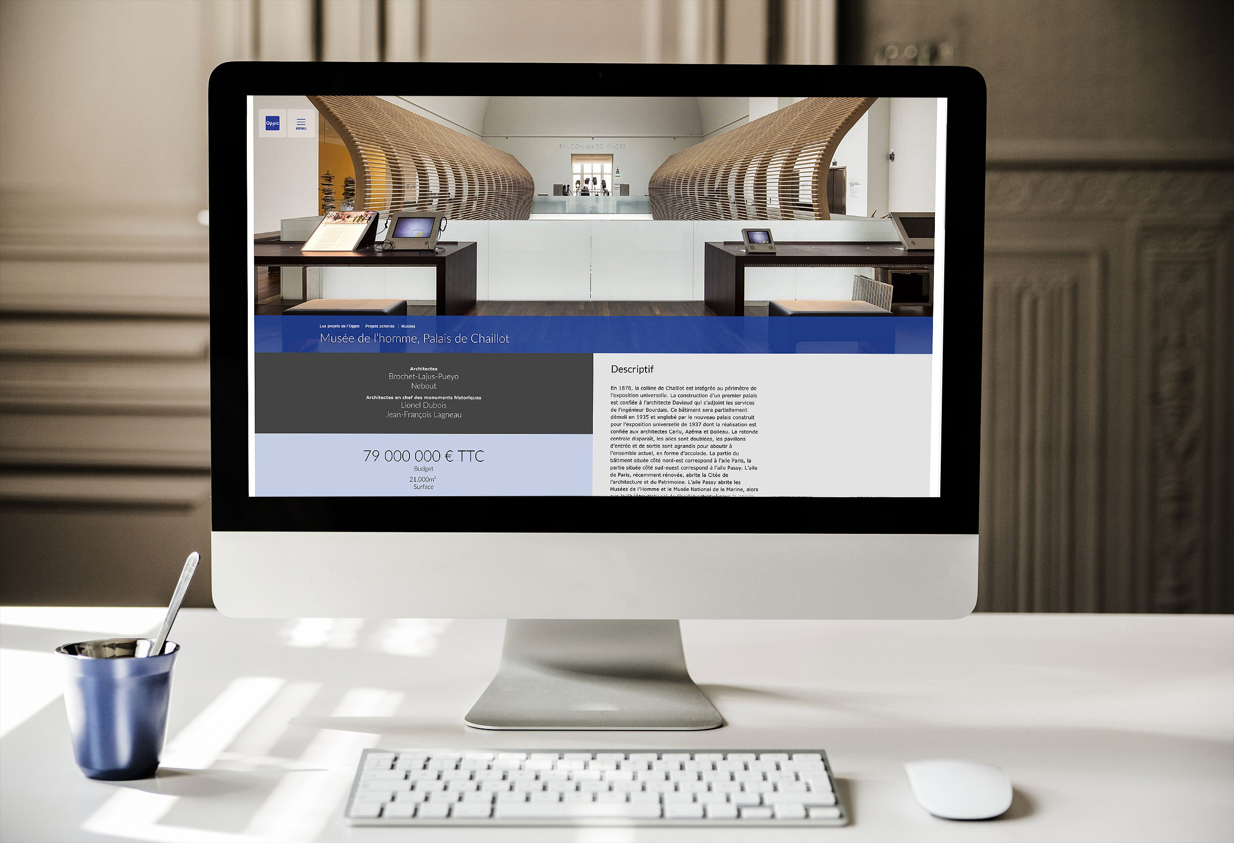 L'image montre un ordinateur de bureau affichant une interface web. L'écran présente un site avec un design moderne, mettant en avant un projet immobilier ou architectural, avec une grande section de texte et des informations financières. On peut apercevoir une table ou un comptoir à l'intérieur d'un espace bien éclairé, probablement un bureau ou une salle d'exposition. Sur le bureau, il y a également une tasse ou un récipient, ce qui ajoute une touche de convivialité à l'environnement de travail.