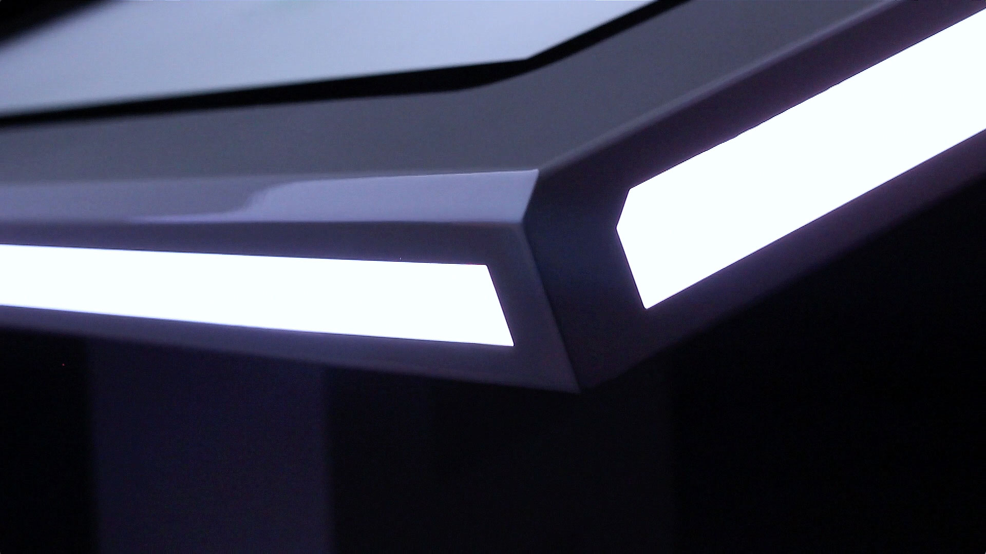 L'image montre un angle d'une surface de bureau ou d'une table moderne, avec un design élégant. La bordure de la table est illuminée par des bandes de lumière blanche, donnant un aspect futuriste et sophistiqué. Le fond est sombre, ce qui met en valeur l'éclairage et les lignes nettes de la table.