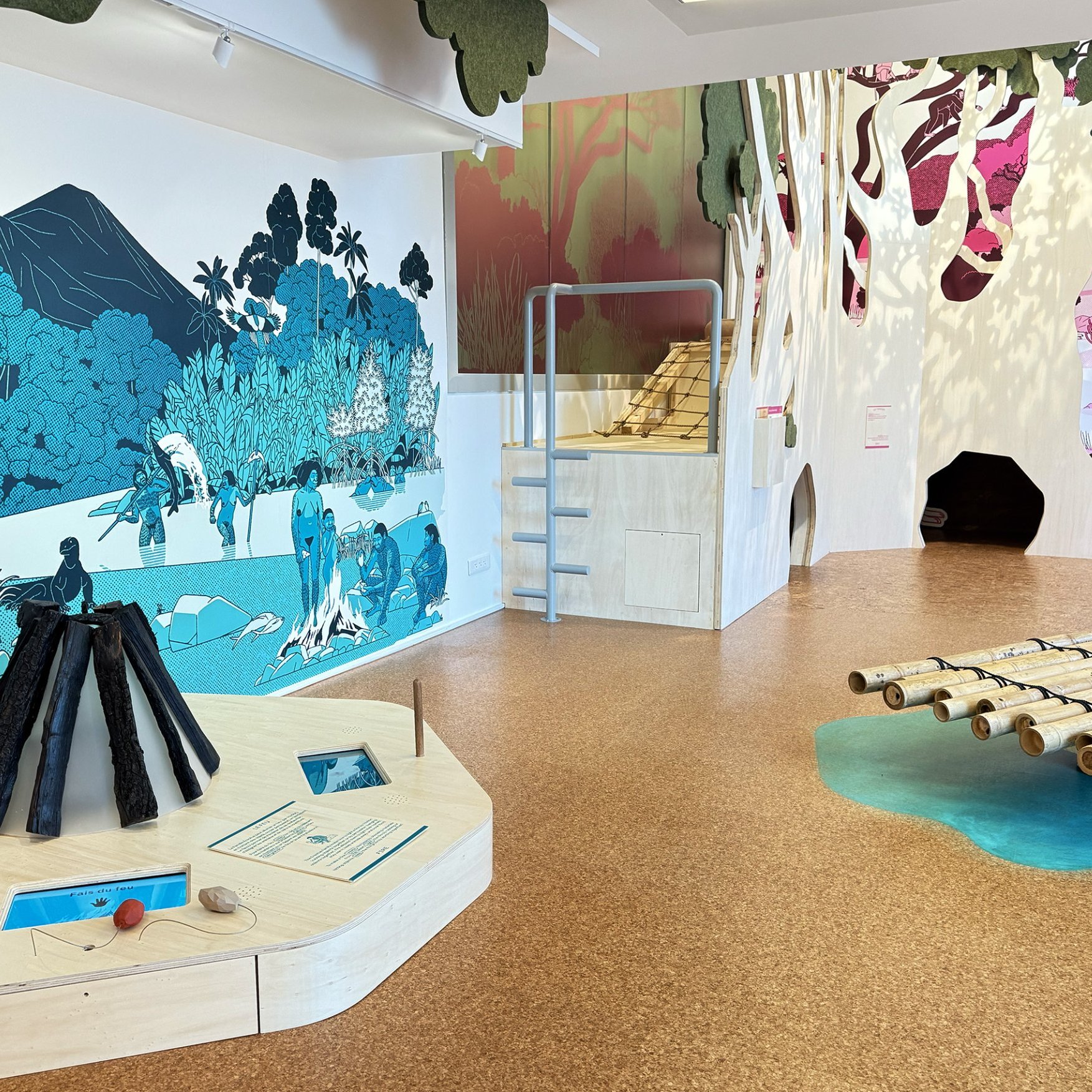 L'image montre un espace d'exposition, probablement dans un musée ou un centre éducatif. On y voit des murs décorés de peintures représentant des paysages et des scènes de la nature. À gauche, il y a une structure en forme de pyramide, faite de matériaux sombres, qui semble être interactive. Au centre, il y a une série de barres en bois disposées à l'horizontale, rappelant un radeau. Le sol est recouvert d'un matériau de couleur claire, et il y a des éléments d'eau stylisés sur le sol. L'ensemble de l'espace semble être dédié à l'exploration de la nature et de l'environnement, avec une approche ludique et éducative.