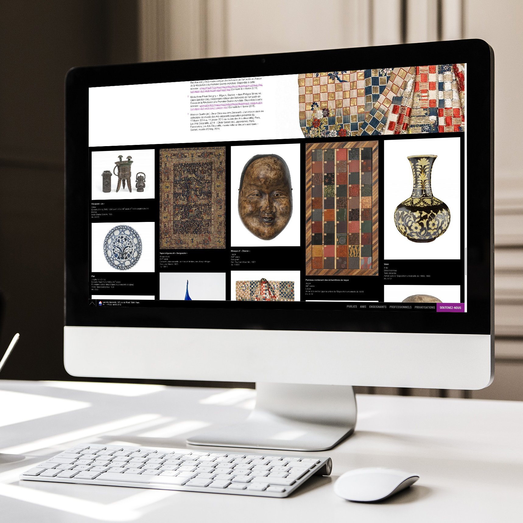 L'image montre un écran d'ordinateur affichant une collection d'objets artistiques ou archéologiques. Sur le fond noir, plusieurs éléments sont disposés : des motifs colorés, des sculptures, des vases et des artefacts ornementaux. Un ordinateur de bureau est posé sur un bureau minimaliste, avec un clavier et une petite tasse en dessous de l'écran. L'environnement semble moderne et épuré, avec un éclairage naturel provenant de la gauche.