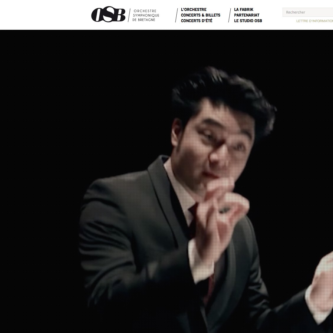 L'image montre un chef d'orchestre en pleine action, vêtu d'un costume sombre, avec un bâton de direction à la main. Son visage exprime une grande concentration et passion, et il semble conduire les musiciens avec dynamisme. L'arrière-plan est flou, mettant en valeur le chef d'orchestre et la scène de concert.