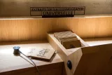L'image montre un espace en bois clair avec une boîte ouverte contenant des cartes ou des planches en bois gravées. Au-dessus de la boîte, il y a un panneau indiquant "EXTRAITS DE LA COSMOGRAPHIE UNIVERSELLE". La lumière douce éclaire doucement le contenu, créant une ambiance chaleureuse et accueillante.