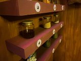 L'image montre des étagères en bois de couleur rose, fixées à un mur en bois. Sur ces étagères, il y a plusieurs bocaux en verre remplis de différentes substances. Certains bocaux contiennent des poudres ou des épices, tandis qu'un autre contient un liquide sombre. Les bocaux sont bien rangés et sont maintenus en place par des supports avec des disques blancs. L'ambiance de la pièce semble chaleureuse et accueillante, avec une touche rustique.