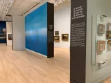 L'image montre l'intérieur d'une galerie d'art spacieuse et moderne. On peut voir des murs peints dans des tons de bleu et de blanc, avec des panneaux d'information imprimés. À gauche, il y a des œuvres d'art accrochées sur le mur, et des éclairages épurés mettent en valeur les tableaux. Le sol est en bois clair, ce qui ajoute une touche chaleureuse à l'espace. L'ensemble évoque une exposition consacrée aux paysages et à l'évolution du genre artistique.