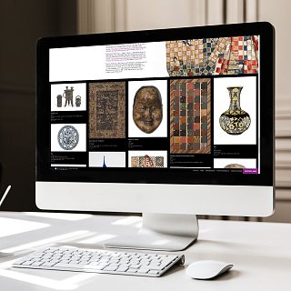 L'image montre un écran d'ordinateur affichant une collection d'objets artistiques ou archéologiques. Sur le fond noir, plusieurs éléments sont disposés : des motifs colorés, des sculptures, des vases et des artefacts ornementaux. Un ordinateur de bureau est posé sur un bureau minimaliste, avec un clavier et une petite tasse en dessous de l'écran. L'environnement semble moderne et épuré, avec un éclairage naturel provenant de la gauche.